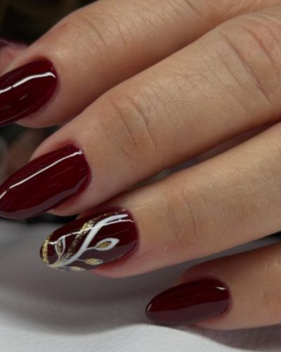 Uñas color vino con diseño de hojas doradas a mano